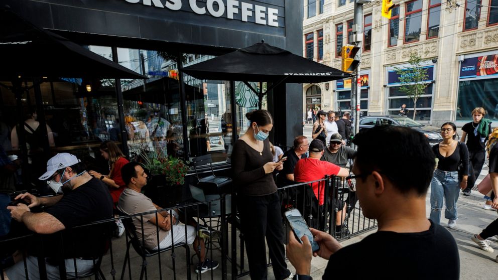 People use electronics outside a coffee shop in Toronto amid a nationwide Rogers outage, affecting many of the telecommunication company's services, Friday, July 8, 2022. (Cole Burston/The Canadian Press via AP)